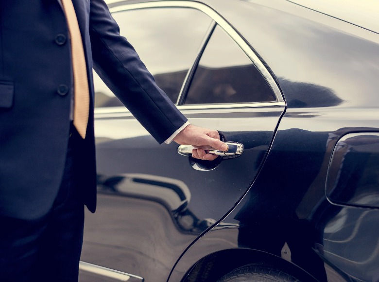 A person wearing a suite opening a car door.