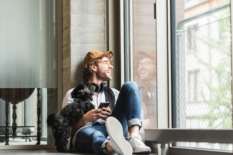 A man with his pet dog at by a window.