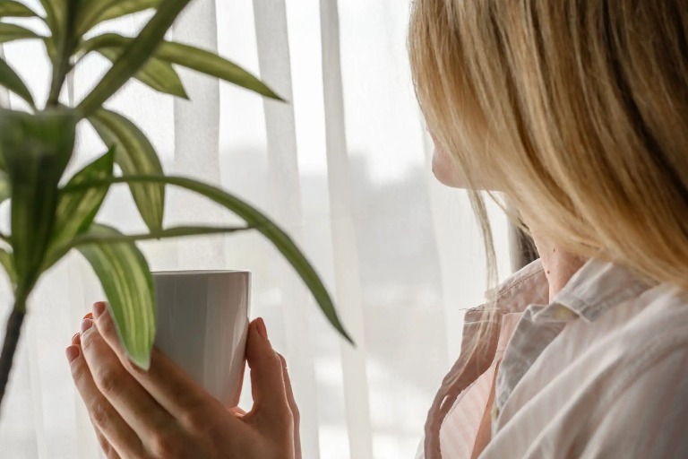 Woman holding a cup and look out the window.