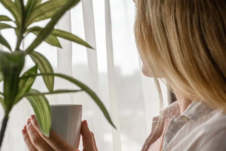 Woman holding a cup and looking out the window.