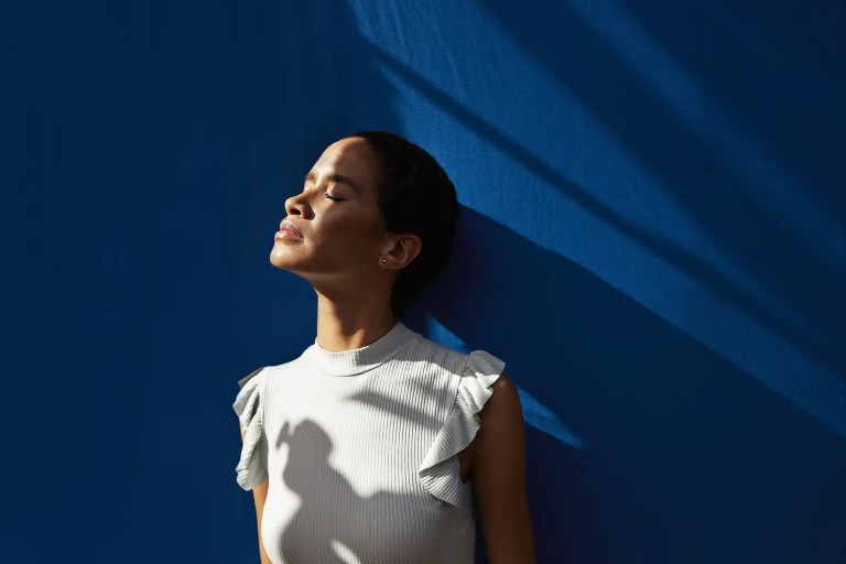 A lady leaning on a blue wall and enjoying the sunshine 