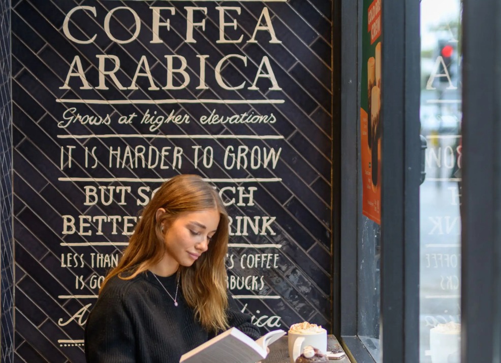 A girl reading a book and enjoying a cup of coffee.