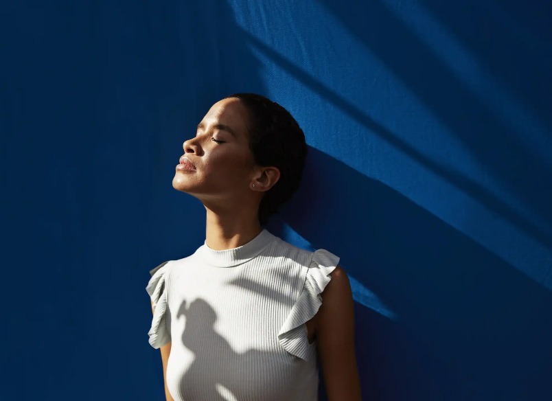 A lady leaning on a blue wall and enjoying the sunshine