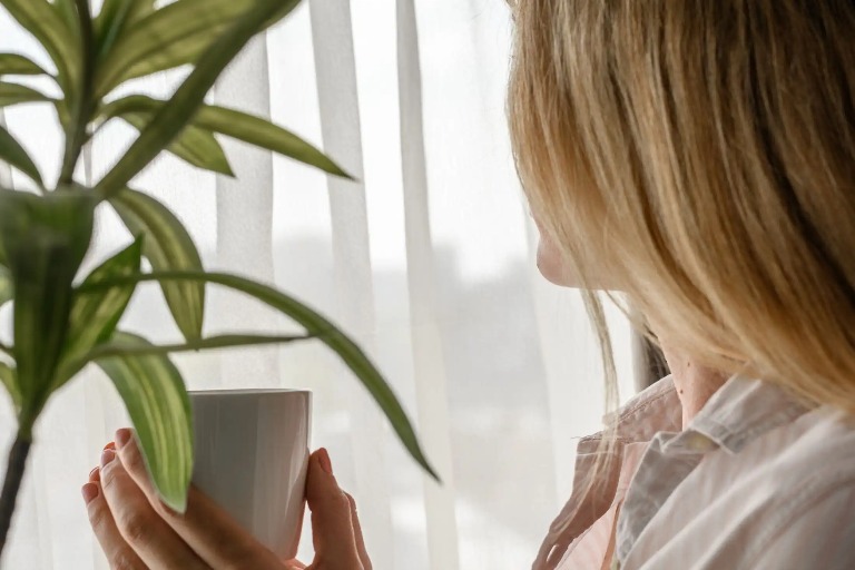 A woman holding a cup and looking out the window.