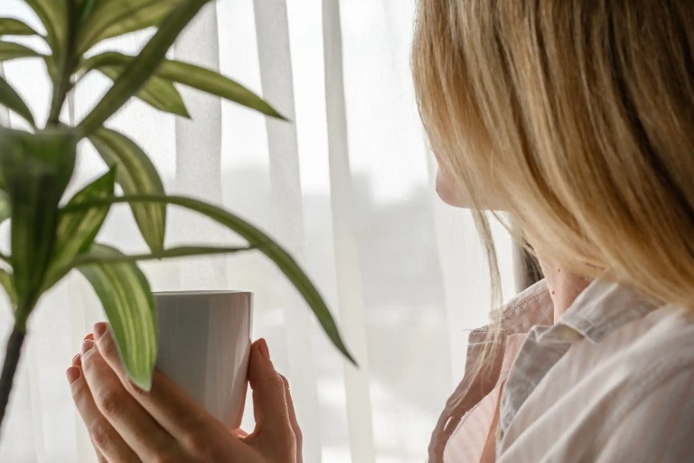 A woman holding a cup and looking out the window.