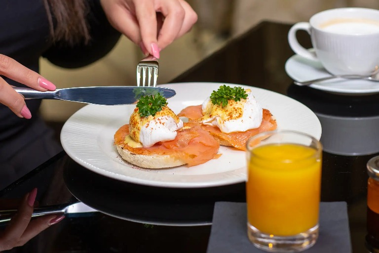 Woman eating eggs benedict and a juice glass beside.