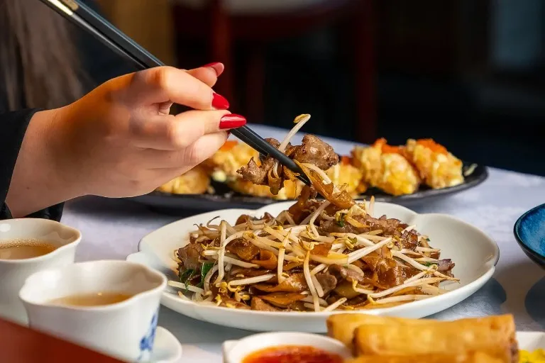 A lady trying out Chinese dishes with chopsticks at Shikumen restaurant at Dao by Dorsett West London Hotel