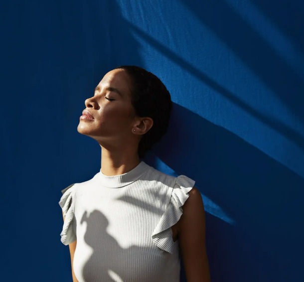 A lady leaning on a blue wall and enjoying the sunshine