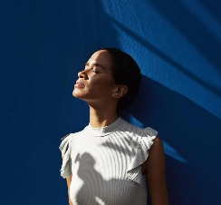 A lady leaning on a blue wall and enjoying the sunshine