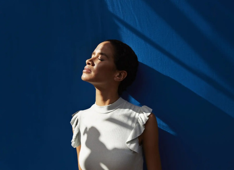 A lady leaning on a blue wall and enjoying the sunshine