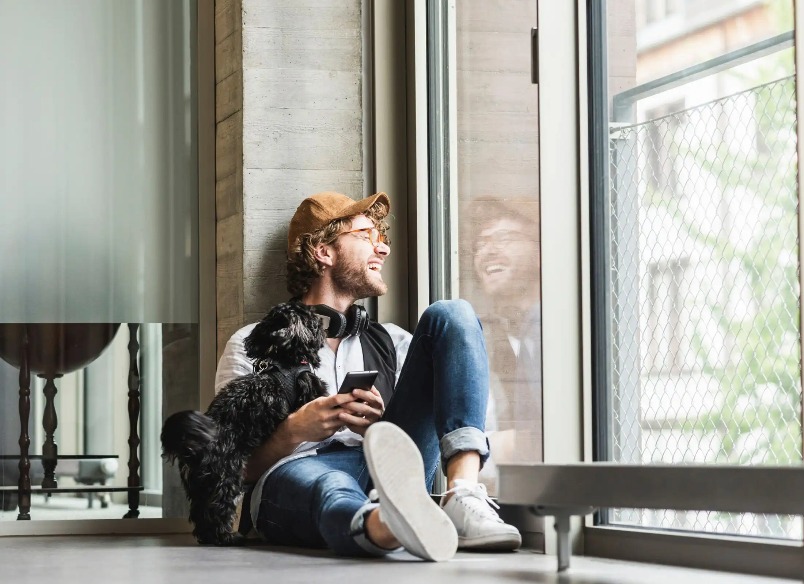 A man with a puppy is looking out the window.