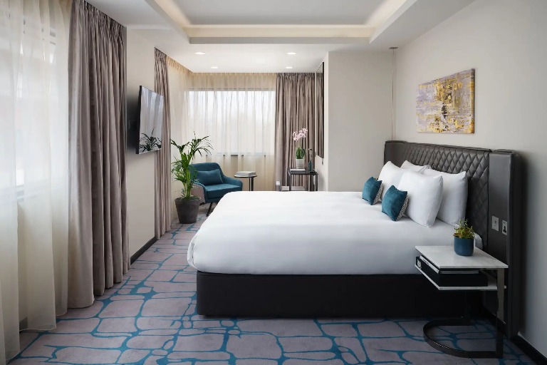 A king-size bed, a working desk and a TV in the Dao Studio Accessible, an accessible hotel room at Dao by Dorsett West London Hotel