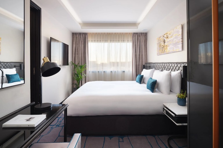 A king-size bed, a wall-mounted TV and a working desk with a lamp in the One-Bedroom at Dao by Dorsett West London Hotel