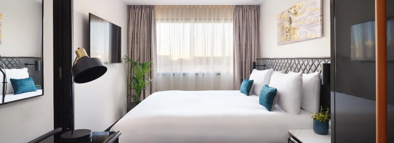 A king-size bed, a wall-mounted TV and a working desk with a lamp in the One-Bedroom at Dao by Dorsett West London Hotel