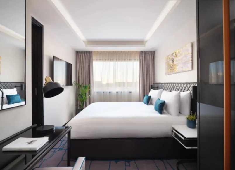 A king-size bed, a wall-mounted TV and a working desk with a lamp in the One-Bedroom at Dao by Dorsett West London Hotel