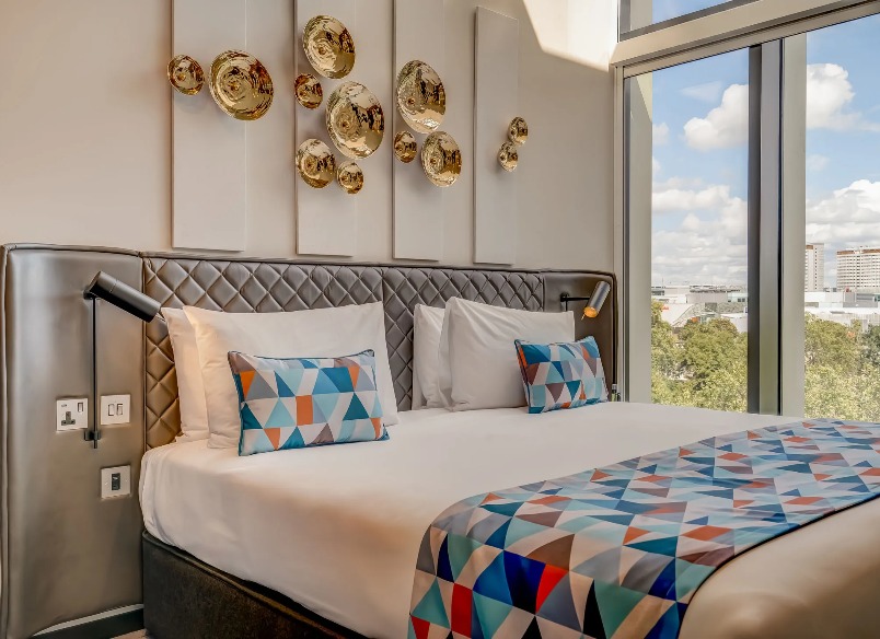 A king-size bed with wall decorations and a view of the city in the Two Bedroom Duplex at Dao by Dorsett West London Hotel